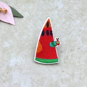 May include: Embroidered patch featuring a red watermelon slice with black seeds and an orange section. A colorful caterpillar is attached to the watermelon. The patch has a white border and green trim.