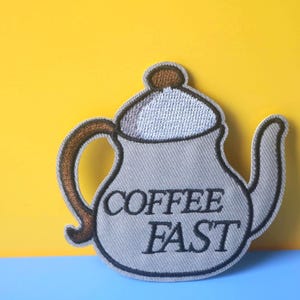 May include: A gray embroidered iron-on patch shaped like a teapot with the text "COFFEE FAST" on it.