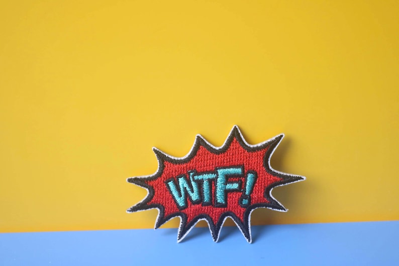 以下が含まれることがあります： 白の感嘆符と青い文字「WTF！」が書かれた、赤と黒の刺繍パッチ