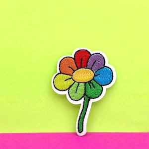 Peut inclure: Écusson de fleur brodée avec un motif de pétales arc-en-ciel, avec des couleurs rouge, orange, jaune, vert, bleu et violet. La fleur a une bordure blanche et une tige verte. Le fond est un mélange vibrant de vert citron et de rose vif.