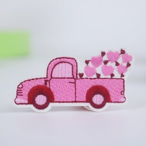 May include: Pink embroidered patch of a pickup truck carrying a bed full of pink hearts.