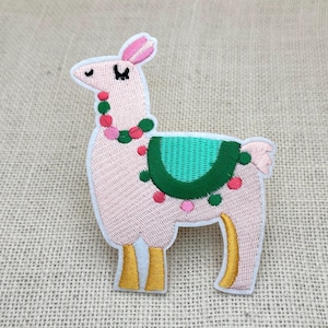 以下が含まれることがあります： 白いアウトラインのピンク色のラマの刺繍パッチ。ラマは緑色のサドル、ピンクと緑のビーズのビーズネックレス、金色の脚を持っています。パッチはベージュ色の生地の背景にあります。