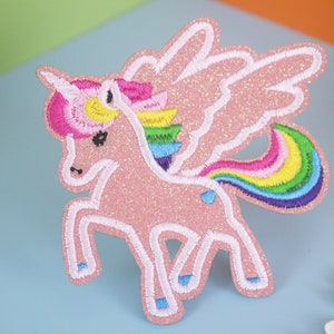 Peut inclure: Patch en forme de licorne rose pailletée avec une crinière et une queue arc-en-ciel, un contour blanc et des ailes.