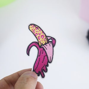 Puede incluir: Un parche de hierro bordado de color rosa y amarillo de un plátano con piel de estampado de leopardo.