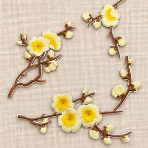 Puede incluir: Tres parches bordados que presentan ramas marrones con flores de color amarillo pálido y centros de color amarillo brillante. Los parches representan ramas florales con capullos y flores abiertas, con costuras detalladas y bordes definidos.