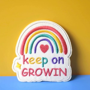 May include: White embroidered patch with a rainbow, a heart, and the text "keep on GROWIN".