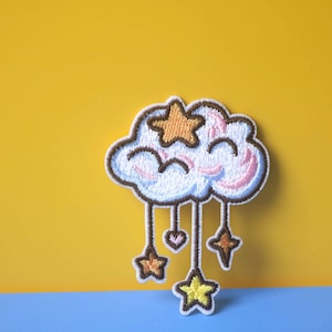 May include: A white cloud with pink and blue accents and a yellow star on top.  The cloud has brown strings hanging from it with a pink heart and yellow stars at the end of each string.