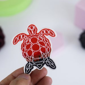 Pode incluir: Patch de ferro bordado vermelho e branco de uma tartaruga marinha.