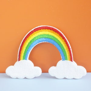 以下が含まれることがあります： 両側に白い雲が付いた虹の刺繍パッチ。虹は赤、オレンジ、黄、緑、青、紫の糸でできています。