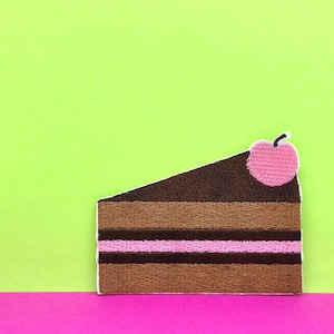 May include: A brown chocolate cake with pink frosting and a pink cherry on top. The cake is on a green and pink background.