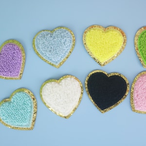 May include: Eight heart-shaped felt patches with gold glitter trim. The patches are in various colors, including light blue, purple, yellow, green, white, black, and pink.