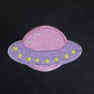May include: A pink and purple embroidered patch of a flying saucer with yellow stars.