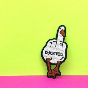 May include: White embroidered patch of a duck giving the middle finger with the text "Duck You" in black.