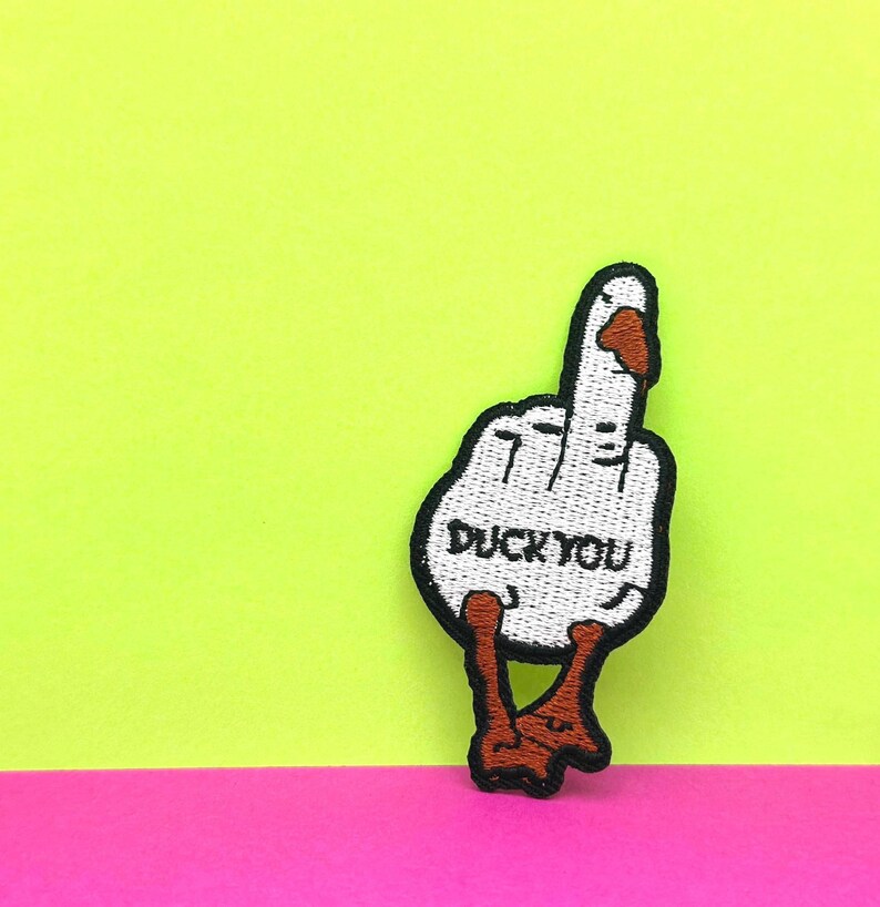 May include: White embroidered patch of a duck giving the middle finger with the text "Duck You" in black.