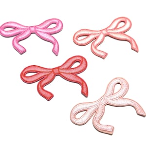 Op de afbeelding: Vier roze, rode en perzikkleurige stoffen strikken. De strikken zijn geborduurd en hebben een 3D-effect.