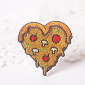 May include: Embroidered patch in the shape of a heart, designed to resemble a slice of pizza. The patch features a golden-brown crust, melted cheese, red pepperoni, green herbs, and white mushroom toppings. The patch has a white border.