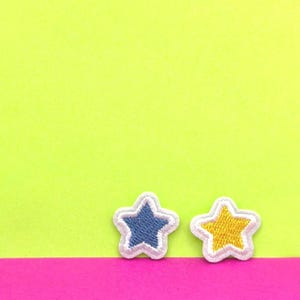 May include: Two embroidered stars, one blue and one yellow, on a green and pink background.