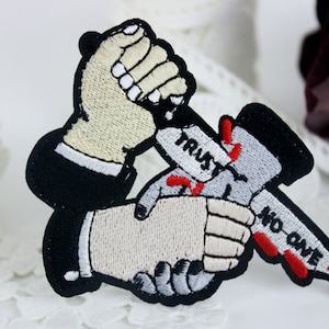 May include: Embroidered patch with two hands shaking, one hand is holding a knife that says "Trust" and the other hand is holding a knife that says "No One".