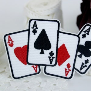 May include: Four white playing card patches with black and red embroidery. The cards are the Ace of Spades, Ace of Hearts, Ace of Diamonds, and Ace of Clubs.