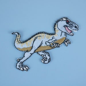 May include: A blue and gold embroidered dinosaur patch with a red eye. The dinosaur is running and has its mouth open.