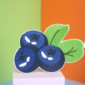May include: Embroidered patch featuring three blue blueberries with green leaves. The patch is ideal for adding a touch of whimsy to clothing, bags, or other crafts.