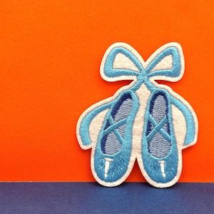 以下が含まれることがあります： 白いリボンが付いた青いバレエシューズの刺繍パッチ