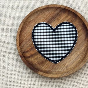 May include: A wooden coaster with a black and white gingham heart design. The coaster is round and made of a light brown wood. The heart is centered on the coaster and has a black border. The background is a light tan burlap.