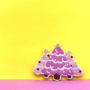 May include: Three pink felt Christmas trees with white stitching and yellow star accents on a yellow background.