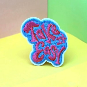 May include: A white embroidered patch with the words "Take it easy" in pink and blue lettering.