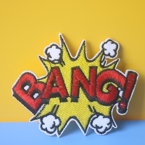 May include: A yellow and red embroidered patch with the word "BANG!" in a comic book style.