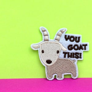 Op de afbeelding: Witte vilt patch met een geborduurde bruine geit en de tekst "YOU GOAT THIS!"