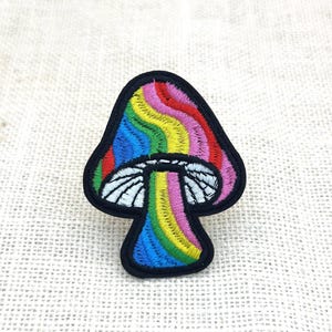 May include: Embroidered mushroom patch with a rainbow design. The mushroom cap features vibrant stripes of red, orange, yellow, green, blue, and purple. The stem is white with black outlines, and the patch has a black border.