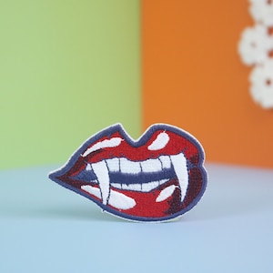 May include: Red embroidered lips with white fangs, a vampire-themed iron-on patch.
