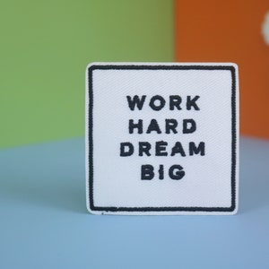 May include: White fabric patch with black embroidered text that reads "Work Hard Dream Big".