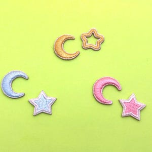 Op de afbeelding: Vijf geborduurde strijkpatches in de vorm van manen en sterren. De patches zijn in tinten roze, blauw en geel.
