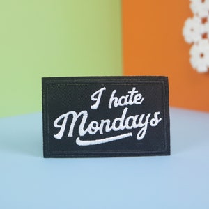 May include: Black embroidered patch with white text that reads "I hate Mondays" on a light blue background.