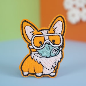 May include: Orange embroidered patch of a cartoon dog wearing a white face mask and goggles.
