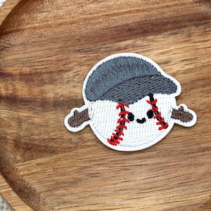 May include: Embroidered baseball patch featuring a smiling baseball character wearing a grey cap. The baseball has red stitching and brown arms. The patch is white with black eyes and a smiling mouth.