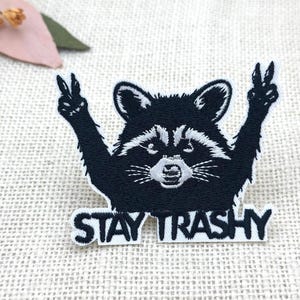 Könnte beinhalten: Eine weiße Keramik-Tasse mit schwarzem Henkel und dem Text "But First, Coffee" in fetter, schwarzer Schrift. Die Tasse steht vor einem verschwommenen Hintergrund. Die Tasse ist etwa 10 cm hoch.