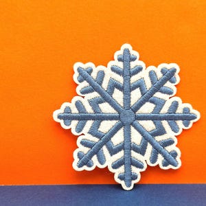 May include: A blue snowflake-shaped embroidered patch with white stitching. The patch is on a bright orange background.