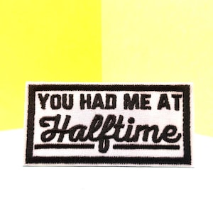 Op de afbeelding: Witte geborduurde patch met zwarte tekst die "You had me at Halftime" luidt.