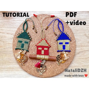 Può includere: Tre ornamenti in macramè fatti a mano a forma di case, ognuno con uno schema di colori diverso: verde, rosso e blu. Gli ornamenti sono appesi a catene dorate e hanno frange dorate. Lo sfondo è un pannello di sughero con il testo "TUTORIAL" e "PDF + video" su di esso. Il testo "NataliDZH made with love" è anche visibile nella parte inferiore dell'immagine.