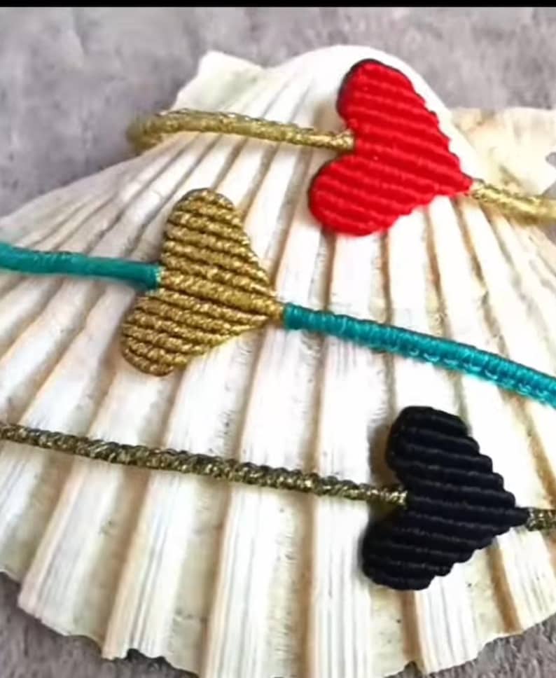 Pode incluir: Tr&ecirc;s pulseiras de amizade com n&oacute;s em forma de cora&ccedil;&atilde;o. As pulseiras s&atilde;o feitas com fio vermelho, dourado e preto.