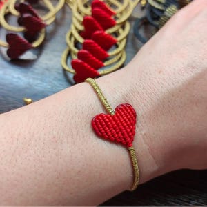 Pode incluir: Um bracelete com um amuleto em forma de cora&ccedil;&atilde;o vermelho feito com fio dourado. O bracelete &eacute; usado no pulso.