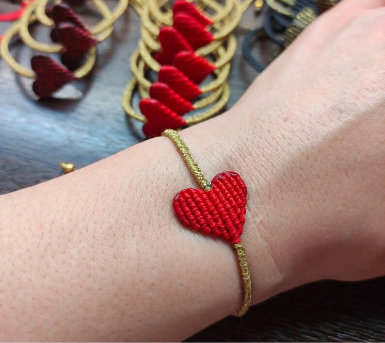 Pode incluir: Um bracelete com um amuleto em forma de cora&ccedil;&atilde;o vermelho feito com fio dourado. O bracelete &eacute; usado no pulso.