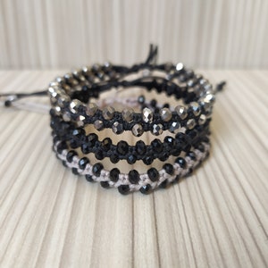 May include: Four layered bracelets with black, silver, and beige beads. The bracelets are made with a string and beads.