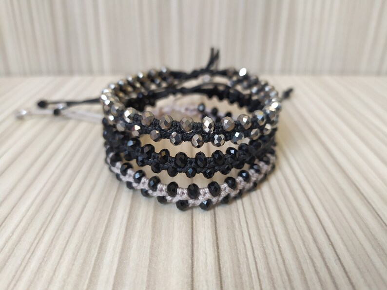 May include: Four layered bracelets with black, silver, and beige beads. The bracelets are made with a string and beads.