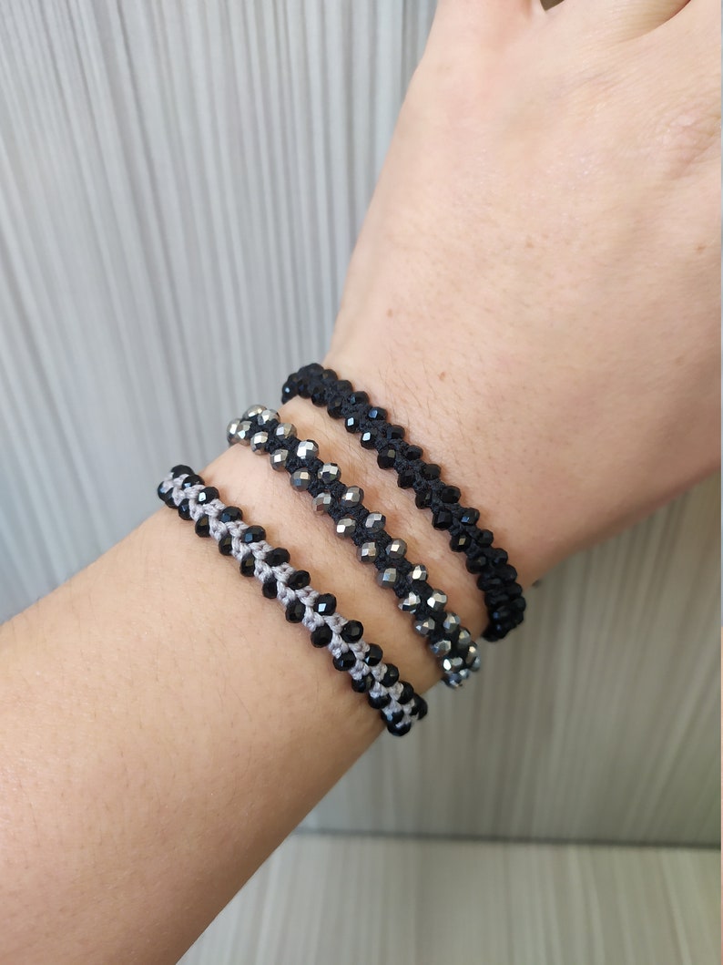 May include: Three beaded bracelets on a wrist. The bracelets are made with black and silver beads and black cord.