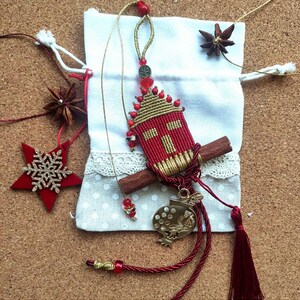 Pu&ograve; includere: Un ornamento natalizio rosso e oro con un design a forma di casa, un bastoncino di cannella e un ciondolo a forma di uccello dorato. L'ornamento &egrave; appeso a un cordino rosso e oro.