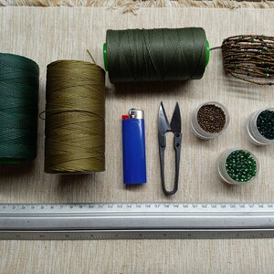 May include: A collection of craft supplies for making jewellery, including two spools of green and brown thread, a lighter, a pair of scissors, a ruler, and four containers of beads in various shades of green and brown.